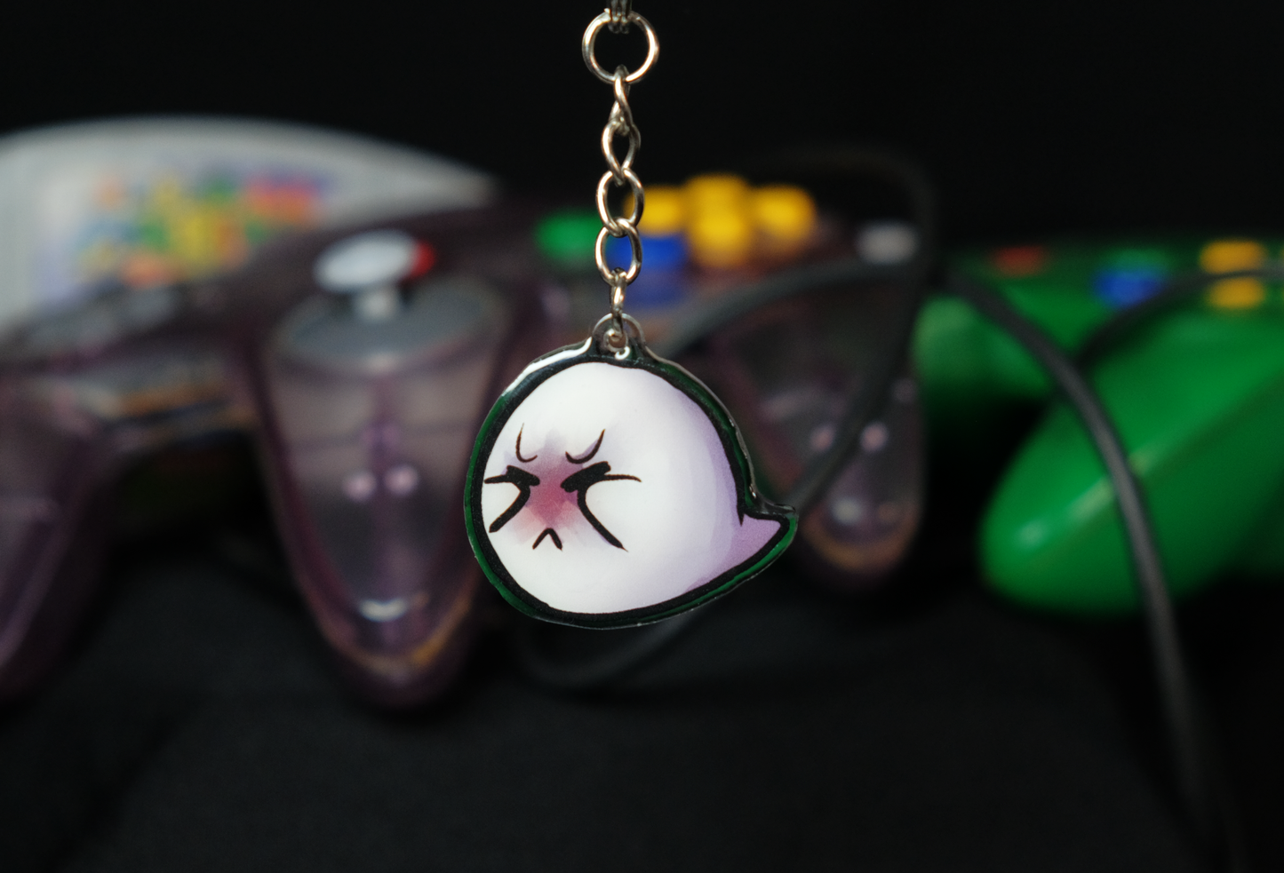 The picture shows a charm of Boo, the ghost from Super Mario, in the center. It is dangling off a key chain. The charm itself is made of clear acrylic.
In the center of the picture is the flipside of the Boo charm on a keychain. The ghost tries to cover half its face with his arms, which are too short. He has his eyes squeezed shut and is turning red in the face.