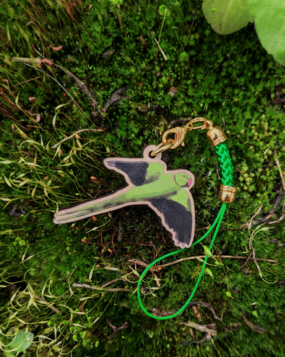 A wooden charm of a rose-ringed parakeet on green moss.